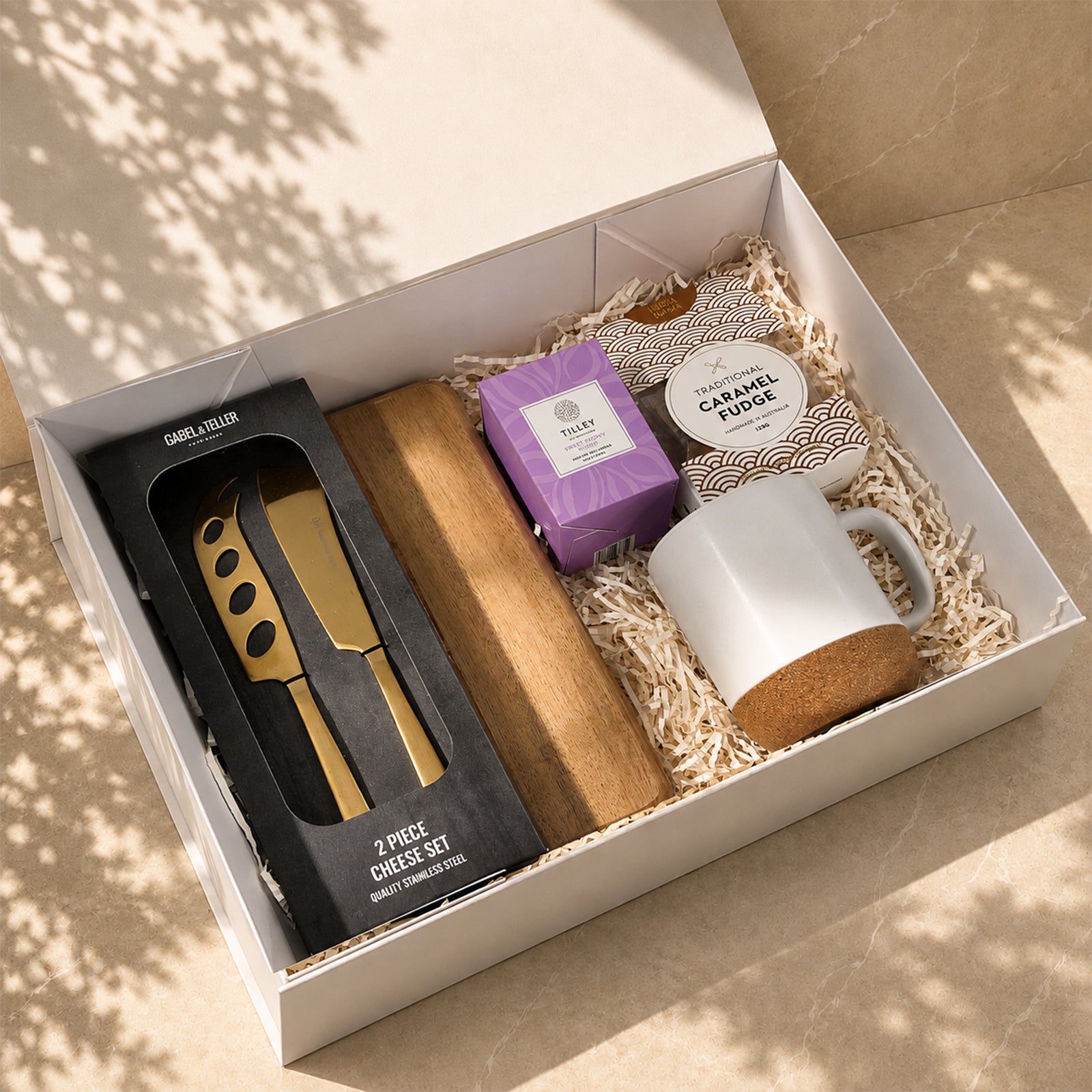 A Little Treat gift box with acacia cheese board, gold cheese knife set, ceramic mug, Tilley candle and caramel fudge in a white box