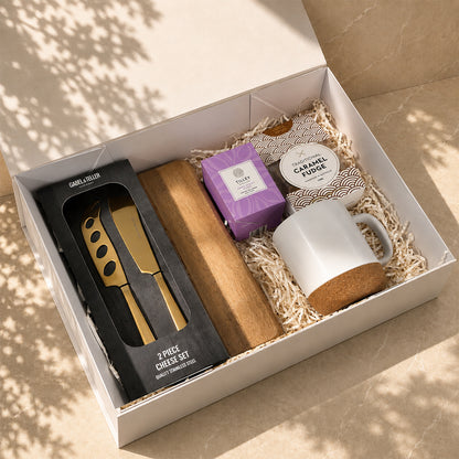 A Little Treat gift box with acacia cheese board, gold cheese knife set, ceramic mug, Tilley candle and caramel fudge in a white box