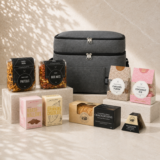 A Whole Lot of Love luxury gift hamper flat lay – grey cooler bag with Chocamama treats, Grounded Pleasure drinking chocolate, marshmallows, VPC crackerthins and fig & almond fruit paste