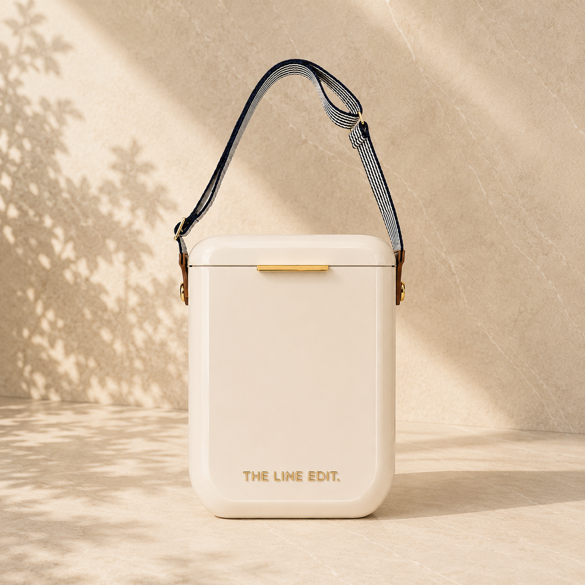 The Line Edit Pavilion cooler in cream, 10 litre hinged lid with a webbing shoulder strap and gold hardware