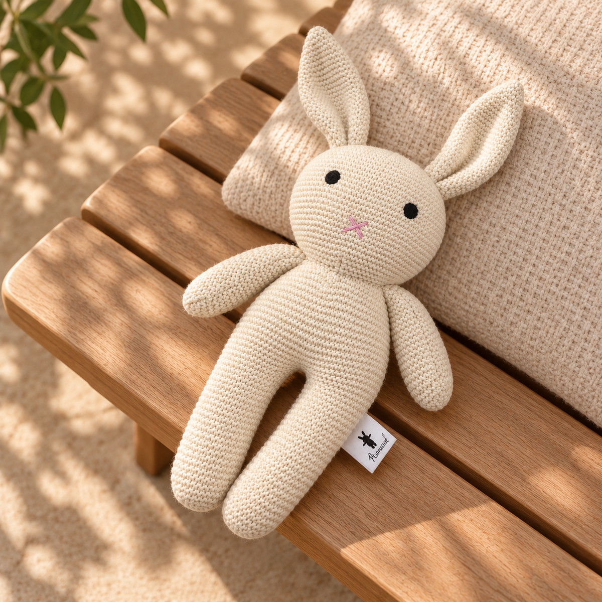 Cream knitted cotton bunny from the Hello Little One baby gift hamper, resting on a sunlit timber stool