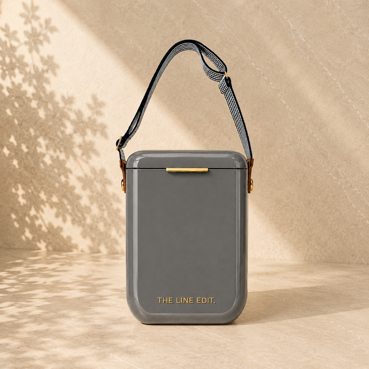 The Line Edit Pavilion cooler in grey, 10 litre hinged lid with a webbing shoulder strap and gold hardware