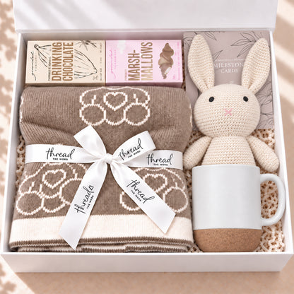 The Cosy Welcome baby gift hamper in Eggshell, teddy bear blanket, bunny, mug, drinking chocolate and marshmallows in a white gift box