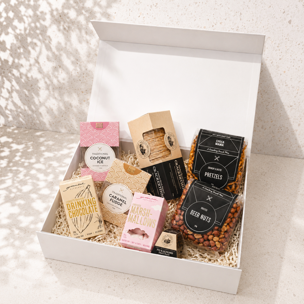 Inside the Gather Around food gift box — open white magnetic gift box filled with Chocamama confectionery, Grounded Pleasures drinking chocolate and marshmallows, Valley Produce Co. crackers, beer nuts and pretzels nestled in vanilla cream paper shred