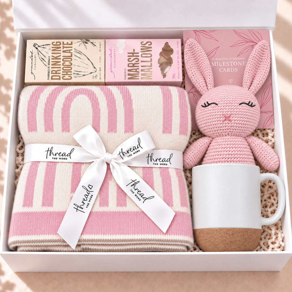 The Cosy Welcome baby gift hamper in Pink, rainbow print blanket, bunny, mug, drinking chocolate and marshmallows in a white gift box