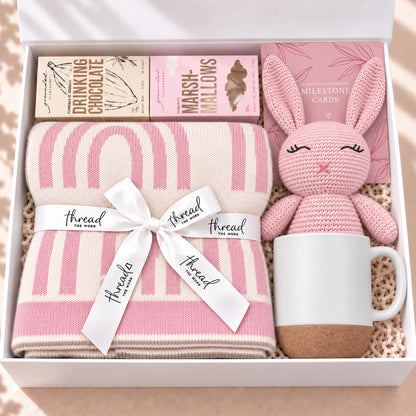 The Cosy Welcome baby gift hamper in Pink, rainbow print blanket, bunny, mug, drinking chocolate and marshmallows in a white gift box