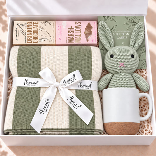 The Cosy Welcome baby gift hamper in Sage, heritage stripe blanket, bunny, mug, drinking chocolate and marshmallows in a white gift box