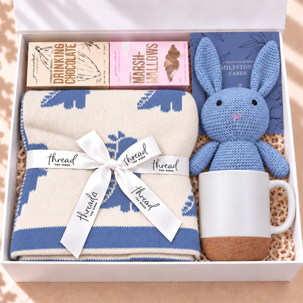 The Cosy Welcome baby gift hamper in Seamist, dinosaur print blanket, bunny, mug, drinking chocolate and marshmallows in a white gift box